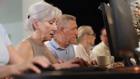 Concerned old woman sitting at computer together with other attendees of IT Video stock 310319785