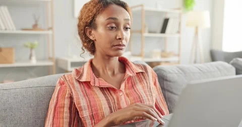Concerned Woman Browsing Laptop While Sitting on Sofa in Bright Modern Home Stock Footage 345390340