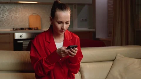 Concerned Woman in Red Blazer Checking Her Phone at Home in the Evening Vídeos de archivo 265214974