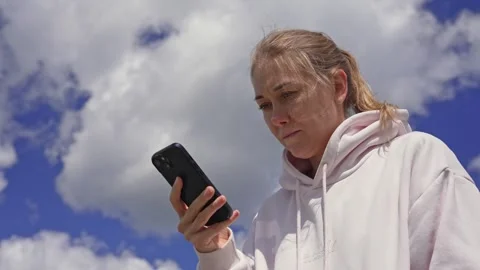 Concerned woman using her mobile phone outdoors under a cloudy sky Stock Footage 338383835
