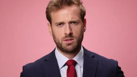 Concerned young elegant man in navy blue suit holding hand to chin and thinking Video stock 137886750