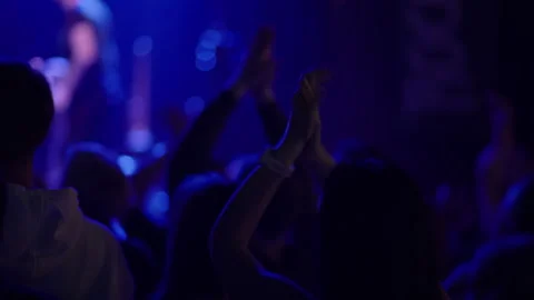 Concert crowd with clapping hands and wristband raised in blue light Stock Footage 334278475