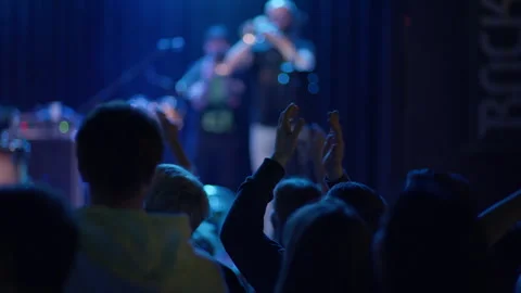 Concert crowd clapping toward stage with guitarist in blue teal light Stock Footage 334278637