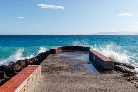 Concreate deck leading into blue ocean with waves crashing. Fotos de archivo