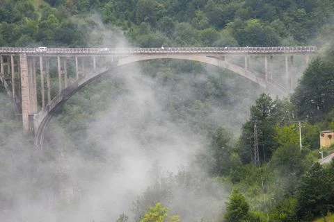 Concrete arch bridge spanning misty forest valley Montenegro Stock Photos