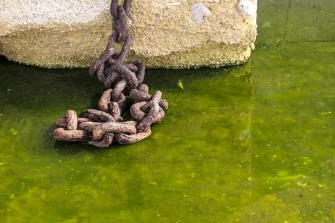 Concrete block with rusty chain on a puddle of green water Stock Photos