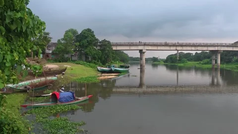 Concrete bridge over river with small wooden boats near bank at dusk Stock Footage 342157719