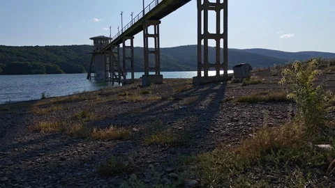 Concrete bridge structure over a calm lake with mountain background Vidéo 312122400