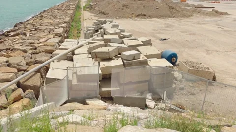 Concrete construction blocks stacked beside rocky seawall at coastal work site Stock Footage 341952521