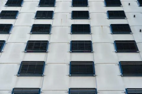 The concrete facade of a prison. The windows are fitted with bars so that the Stock Photos