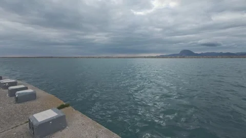 Concrete Pier Edge With Seats Facing Open Sea and Distant Island Stock Footage 338108385