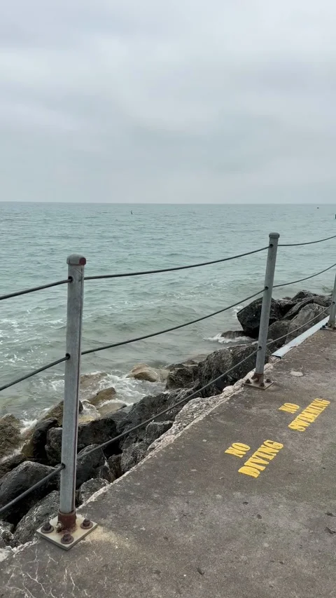 Concrete pier marked “NO DIVING” as waves crash against the rocks below 库存影片 342336641