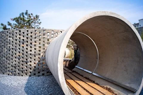 Concrete pipe intersecting a brick lattice wall - Architecture concept Stock Photos