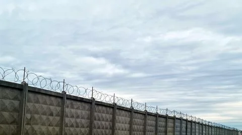 Concrete security wall with barbed wire against cloudy sky Stock Photos