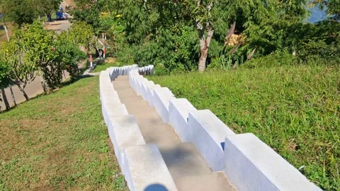 Concrete steps on grassy hill with trees and people in background Vídeo Stock 331655800