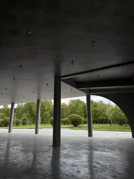Concrete structure with columns and ceiling lights, open view towards green Stock Photos