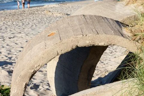 Concrete structure on a sandy beach with people walking in the background Stock Photos