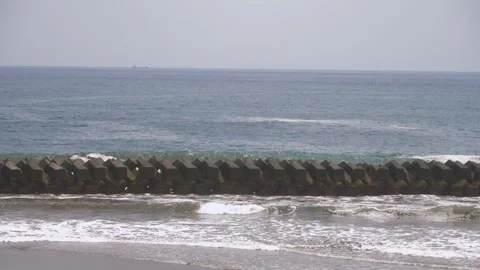Concrete tetrapod breakwater lining a sandy beach with a cargo ship on the Stock Footage 345176975