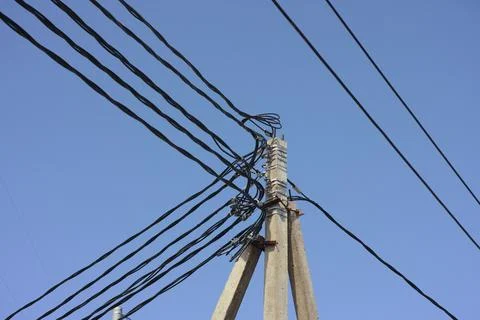 A concrete utility pole with a complex tangle of black electrical power lines 库存照片