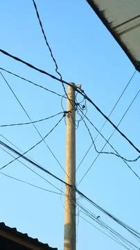Concrete utility pole with intersecting power lines against blue sky Stock Photos