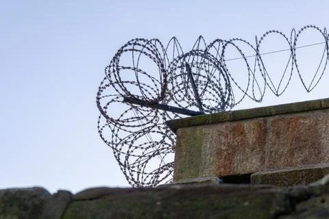 Concrete wall with barbed wire, view from below against the sky. The top edge of Stock Photos
