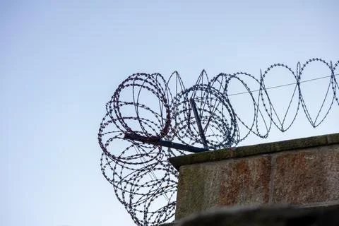 Concrete wall with barbed wire, view from below against the sky. The top edge of Stock Photos