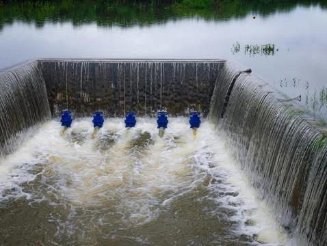 A concrete weir structure controls water flow in a rural river Stock Photos