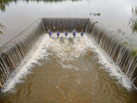 A concrete weir structure controls water flow in a rural river Stock Photos