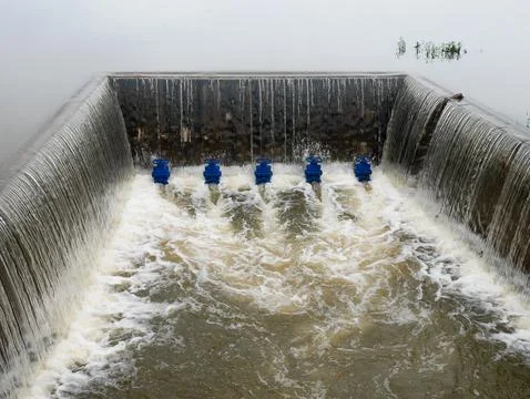 A concrete weir structure controls water flow in a rural river Stock Photos