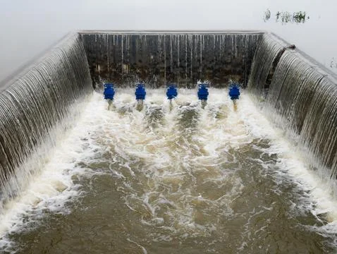 A concrete weir structure controls water flow in a rural river Stock Photos