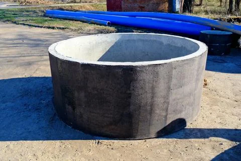 Concrete well ring on construction site with blue plastic pipes utility inf.. 库存照片