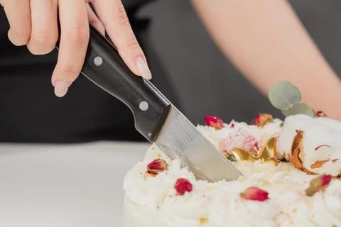 A condater cuts a beautiful fresh decorated white cake with a large knife. Stock Photos