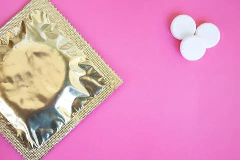 A condom in foil pack and three tablets on pink background with copy space Stock Photos