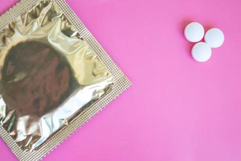 A condom in foil pack and three tablets on pink background with copy space Stock Photos