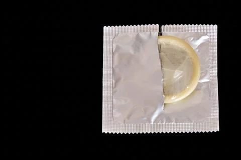 A condom is half pulled out of an open package on a dark background. Top vi.. Stock Photos