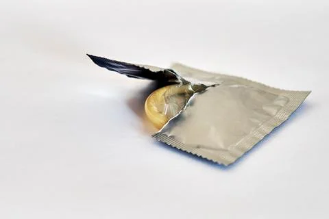 Condom half pulled out of the open package on a white background. Side view. Stock Photos