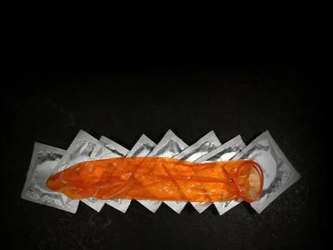 Condom stretch open placed on packets on textured black background with copy Stock Photos