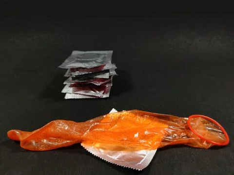 Condom stretch open placed on packets on textured black background with copy Foto stock