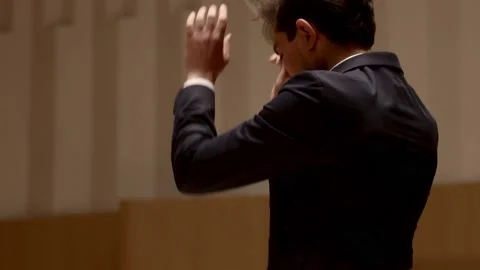 Conductor of symphony orchestra with performers in background in concert hall Stock Footage 199556179