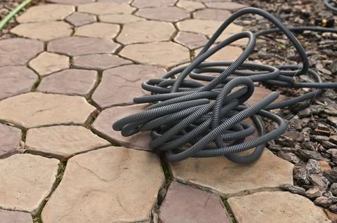 Conduit lying coiled on paving stone surface outdoors. Conduit made of flex.. Stock Photos