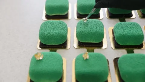 Confectioner adding an edible gold colored foil decor element to the top of cake Stock Footage 134681380