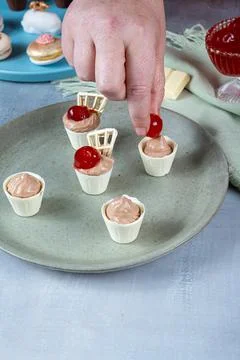 Confectioner decorating with cherry, small white chocolate cups filled with m Stock Photos
