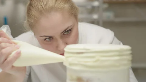 Confectioner decorating rotating cake using pastry bag with cream. Bakery Stock Footage 170047308