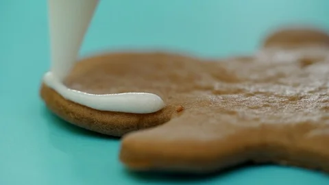 A confectioner is drawing a contour on ginger biscuits by white icing with using Stock Footage 99705980