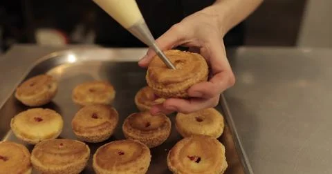 The confectioner fills the eclair with cream using a pastry syringe. Female.. Stock Photos