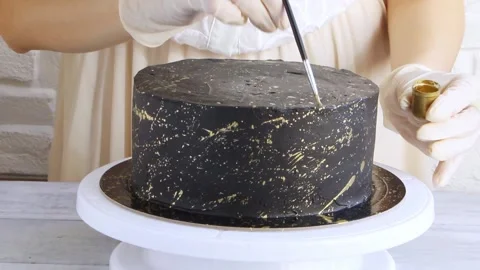 Confectioner paints gold splashes on black cake. Close up Stock Footage 150332260