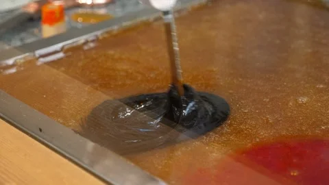 The confectioner pours the dye into the liquid caramel and mixes it with a stick Stock Footage 330869663