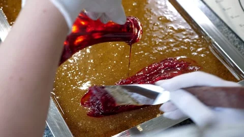 The confectioner pours the dye into the liquid caramel and mixes it with a stick Stock Footage 330869969