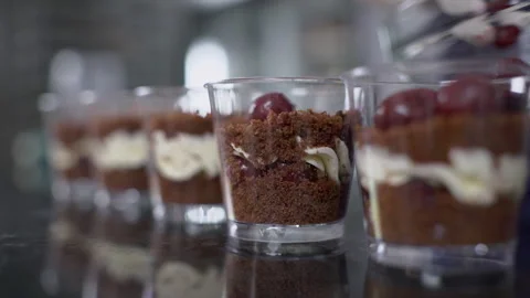 Confectioner puts cherry in cups with layered cakes in kitchen indoors. Stock Footage 85617696