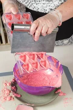 Confectioner using a spatula to remove excess strawberry ganache in a polycar Stock Photos